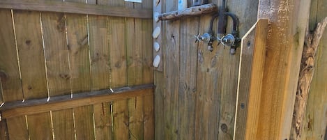Et udendørs bruseområde i træ med en ståldør, et træhegn og en sort måtte på gulvet.