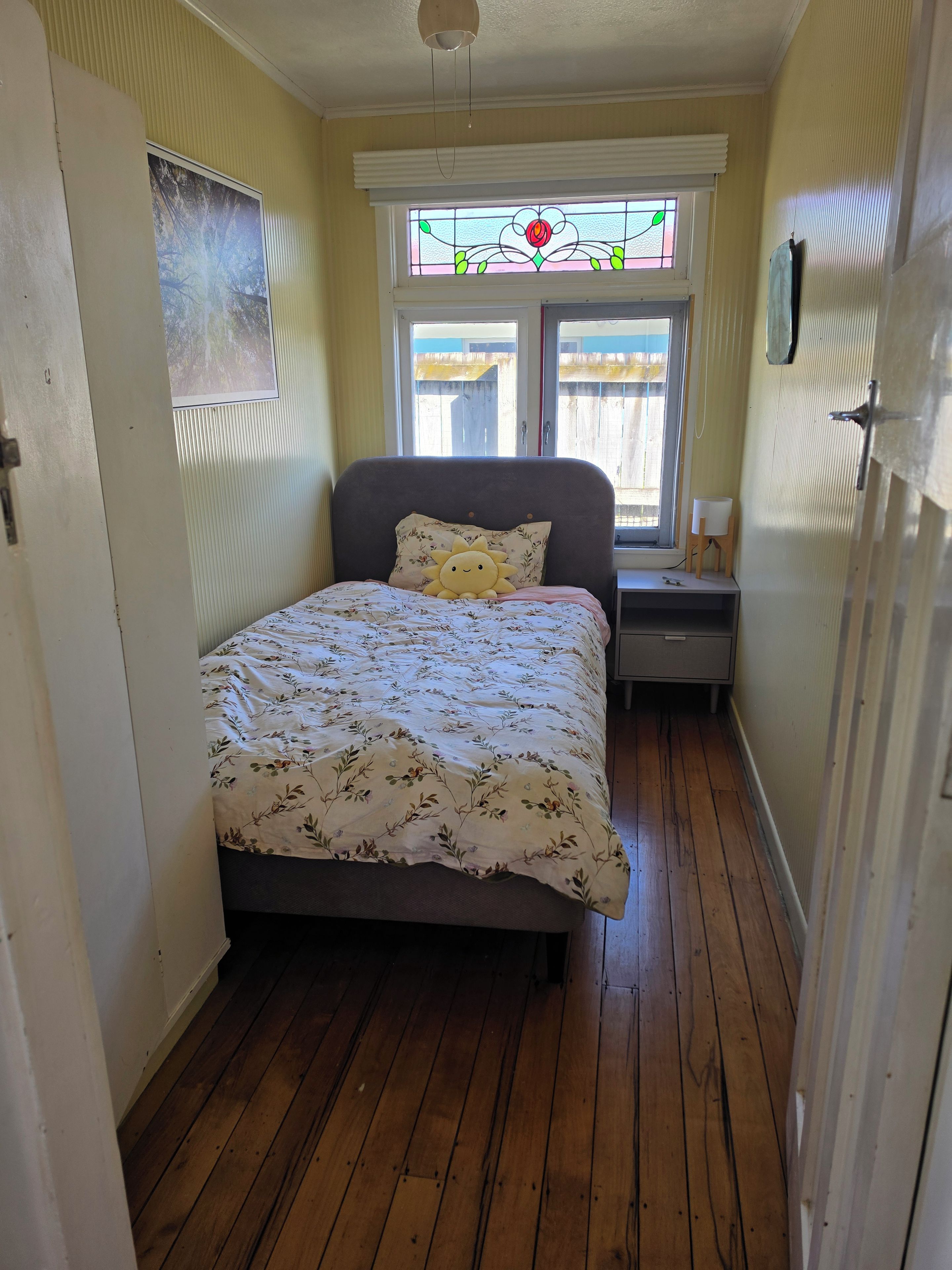 Une chambre à coucher comprenant un lit, une table de chevet, une fenêtre ornée de vitraux et une porte.