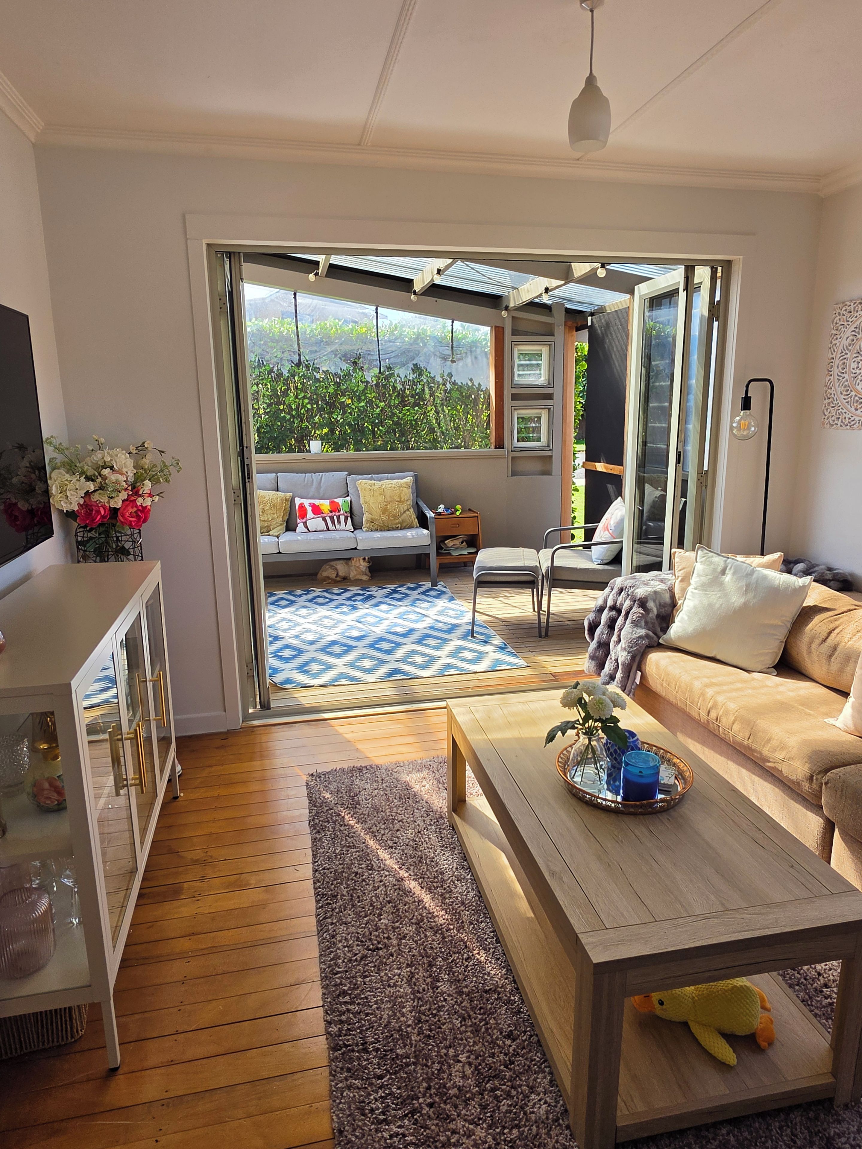 A modern living room with a sofa, coffee table, and a view of a garden through a glass door.