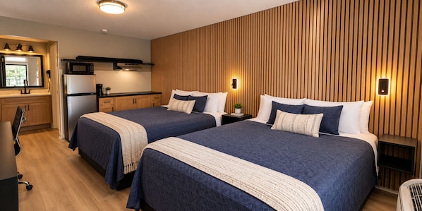 Habitació d'hotel amb dos llits, una petita cuina i panells de paret de fusta.