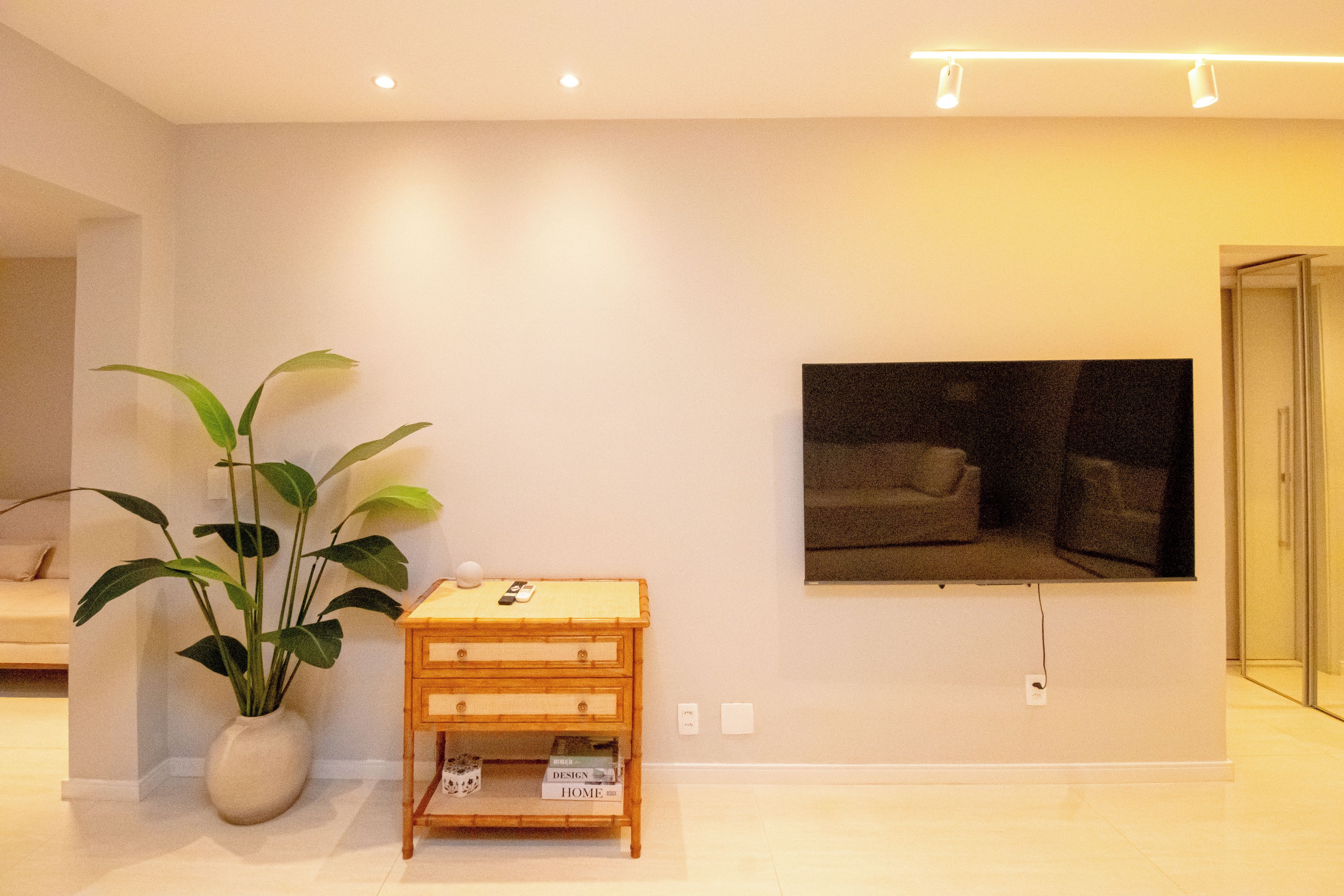 Ein modernes Wohnzimmer mit einer großen Topfpflanze, einem Holztisch mit Büchern, einem flachbildfernseher an der Wand und einem minimalistischen Design.
