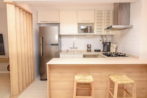 A modern kitchen with a stainless steel refrigerator, a microwave, a coffee maker, and a gas stove. There are two wooden stools at the counter. - New Listing (Rio de Janeiro)