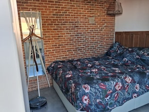 A room with a brick wall, a bed with floral bedding, a mirror, and a hanging light fixture. - New Listing (Madrid)