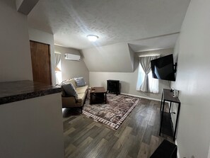 A compact living space with a sofa, a flat-screen TV mounted on the wall, and a small table. - CatalpaCorner Peace-filled/Sky-Haven/Turnkey/Mid-term/Monthly/Weekly (Springfield)