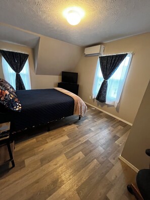A bedroom with a bed, a TV, an air conditioning unit, and a window with curtains. - CatalpaCorner Peace-filled/Sky-Haven/Turnkey/Mid-term/Monthly/Weekly (Springfield)