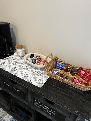 A kitchen area with a coffee maker, a plate of food, and a basket of snacks on a table. - CatalpaCorner Peace-filled/Sky-Haven/Turnkey/Mid-term/Monthly/Weekly (Springfield)