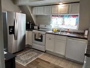 A modern kitchen with stainless steel appliances, white cabinetry, and a window with a floral curtain. - CatalpaCorner Peace-filled/Sky-Haven/Turnkey/Mid-term/Monthly/Weekly (Springfield)