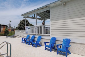 A covered outdoor seating area with blue Adirondack chairs, a white building with a balcony, and a pool sign indicating no diving. - Simply Serenity-Lakefront-Pet Friendly-Heated Pool (Destin)