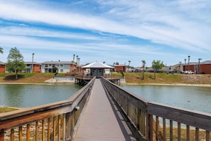 A wooden boardwalk leading to a building with a covered area, surrounded by water and palm trees. - Simply Serenity-Lakefront-Pet Friendly-Heated Pool (Destin)