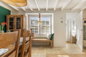A room with a wooden dining table, chairs, a bench with a cushion, a hanging light fixture, a window with blinds, and a radiator. - The Gables - Sea Views Rustic Country Charm (Newport)