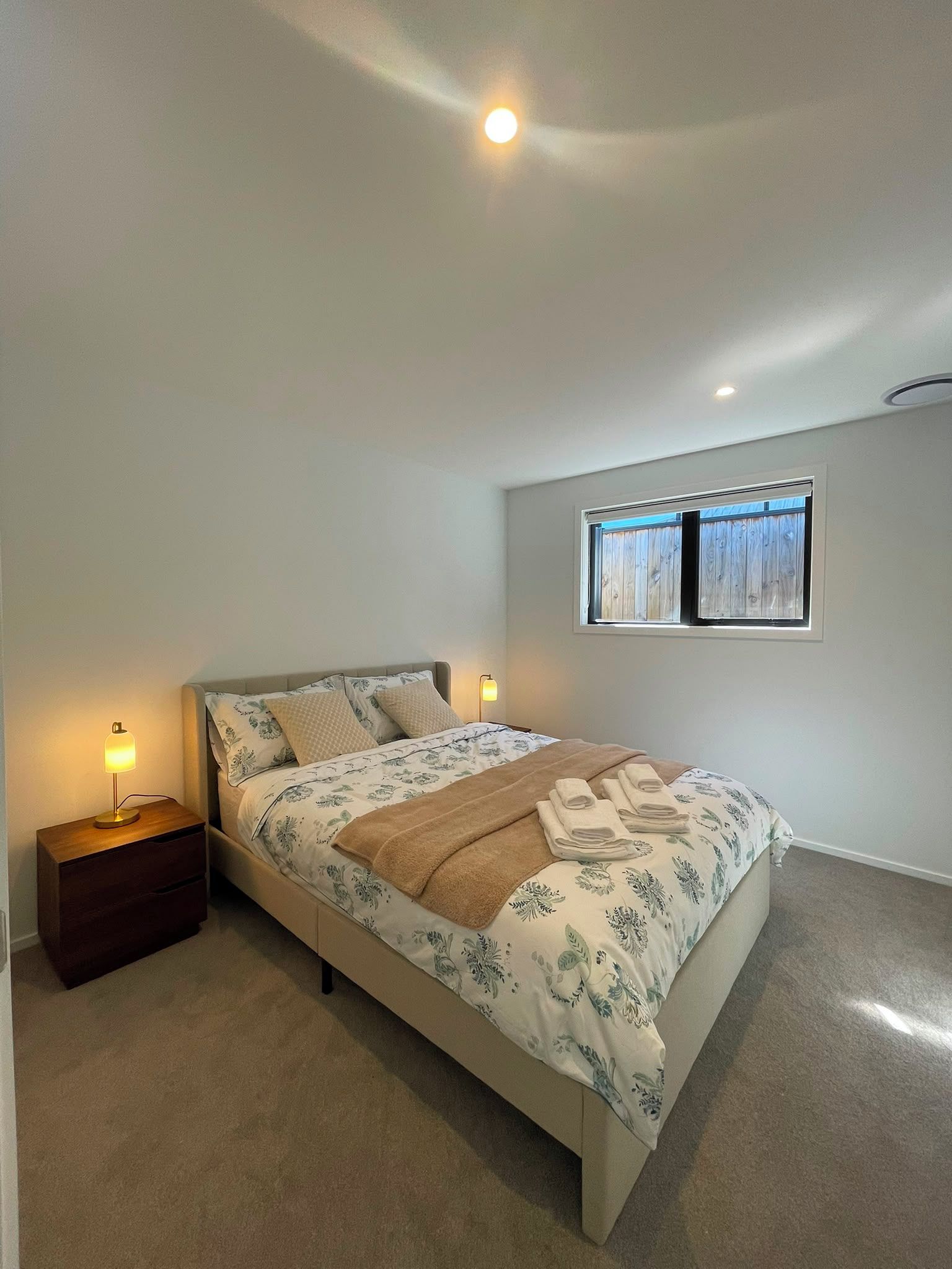 Une chambre à coucher avec un lit, une table de chevet, une lampe et une fenêtre.
