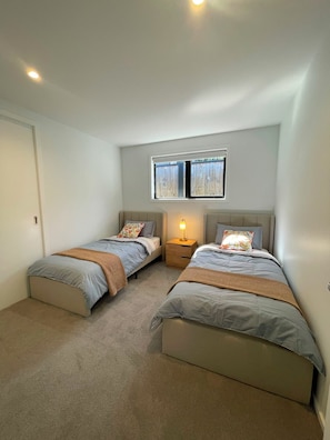 Une chambre avec deux lits, une table de chevet, une fenêtre et une porte.