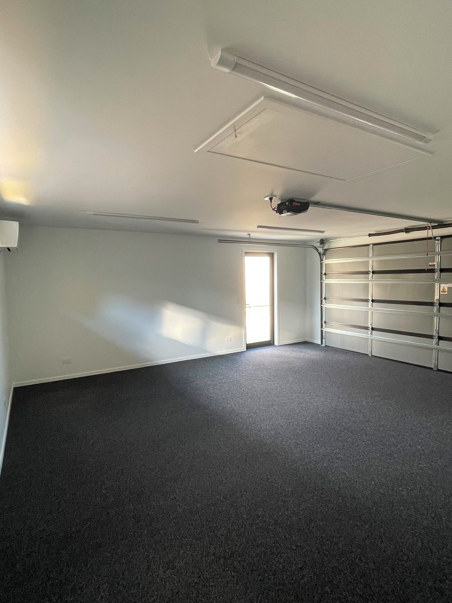 Une pièce avec un tapis gris, un ventilateur de plafond et une étagère métallique adossée au mur.