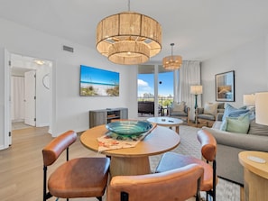 Ein modernes Wohnzimmer mit einem runden Holztisch, Ledersesseln, einer Couch und einem Balkon mit Blick auf den Strand.