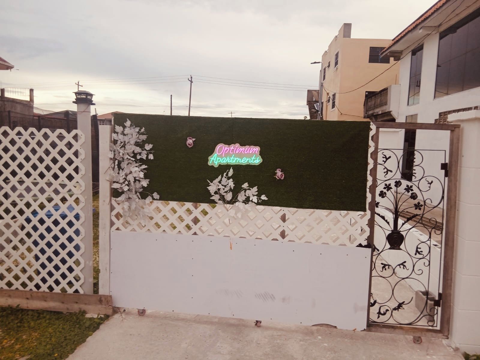 A gated entrance with a neon sign for 'Optimum Apartments' and a decorative metal gate.