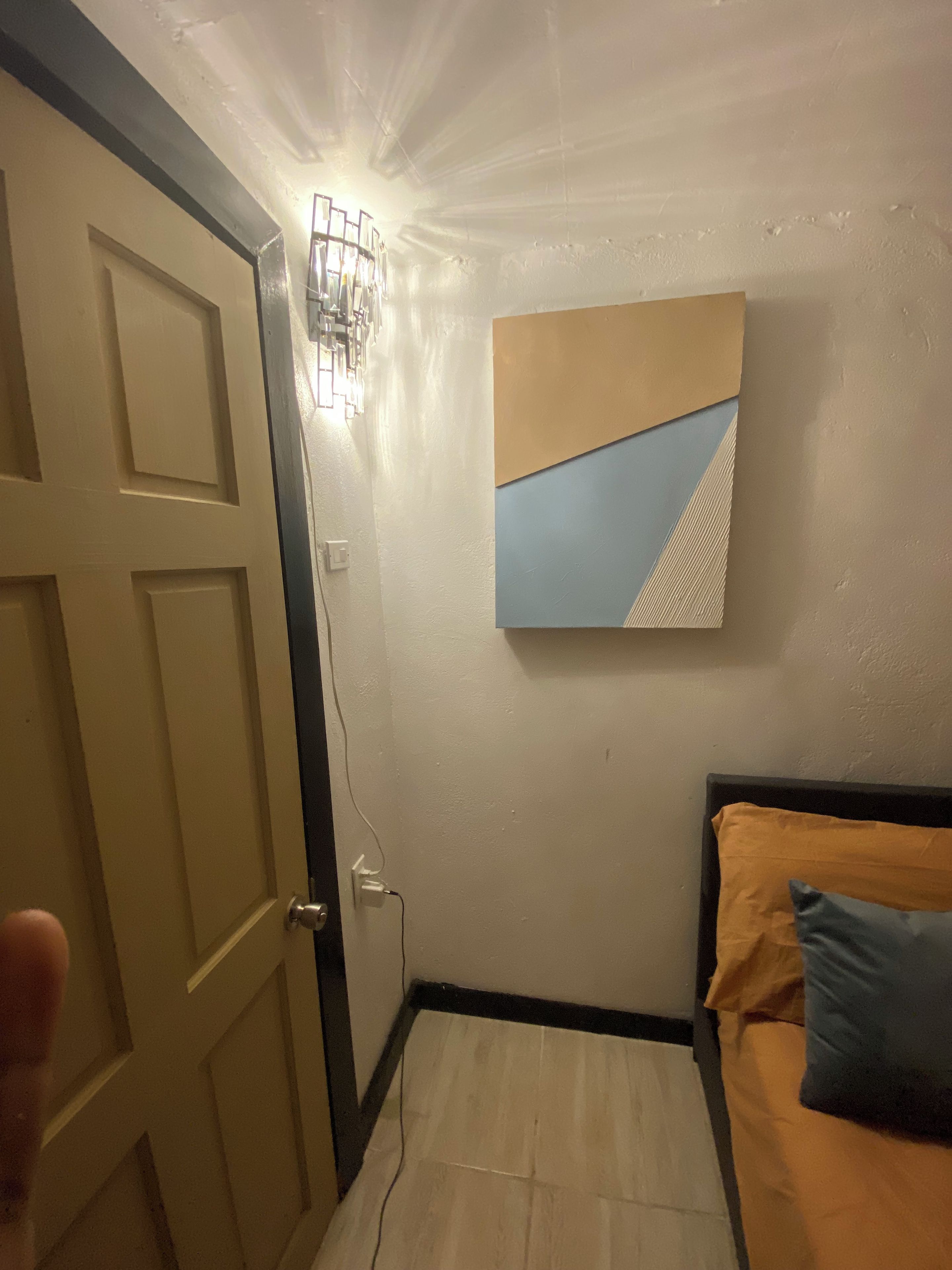 A bedroom with a bed, a wall-mounted light fixture, and a painting.