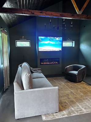 A modern living room with a white sofa, a dark armchair, a fireplace, and a large TV screen displaying a beach scene.