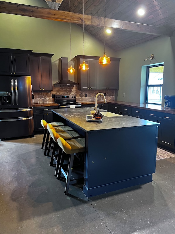 A modern kitchen with a central island, bar stools, a stainless steel refrigerator, and pendant lighting.