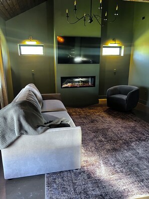 Een moderne woonkamer met een bank, een fauteuil, een flatscreen televisie aan de muur en een kamerkleed met een patroon.