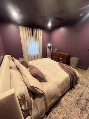 A bedroom with a bed, a dresser, a mirror, and a window with curtains.