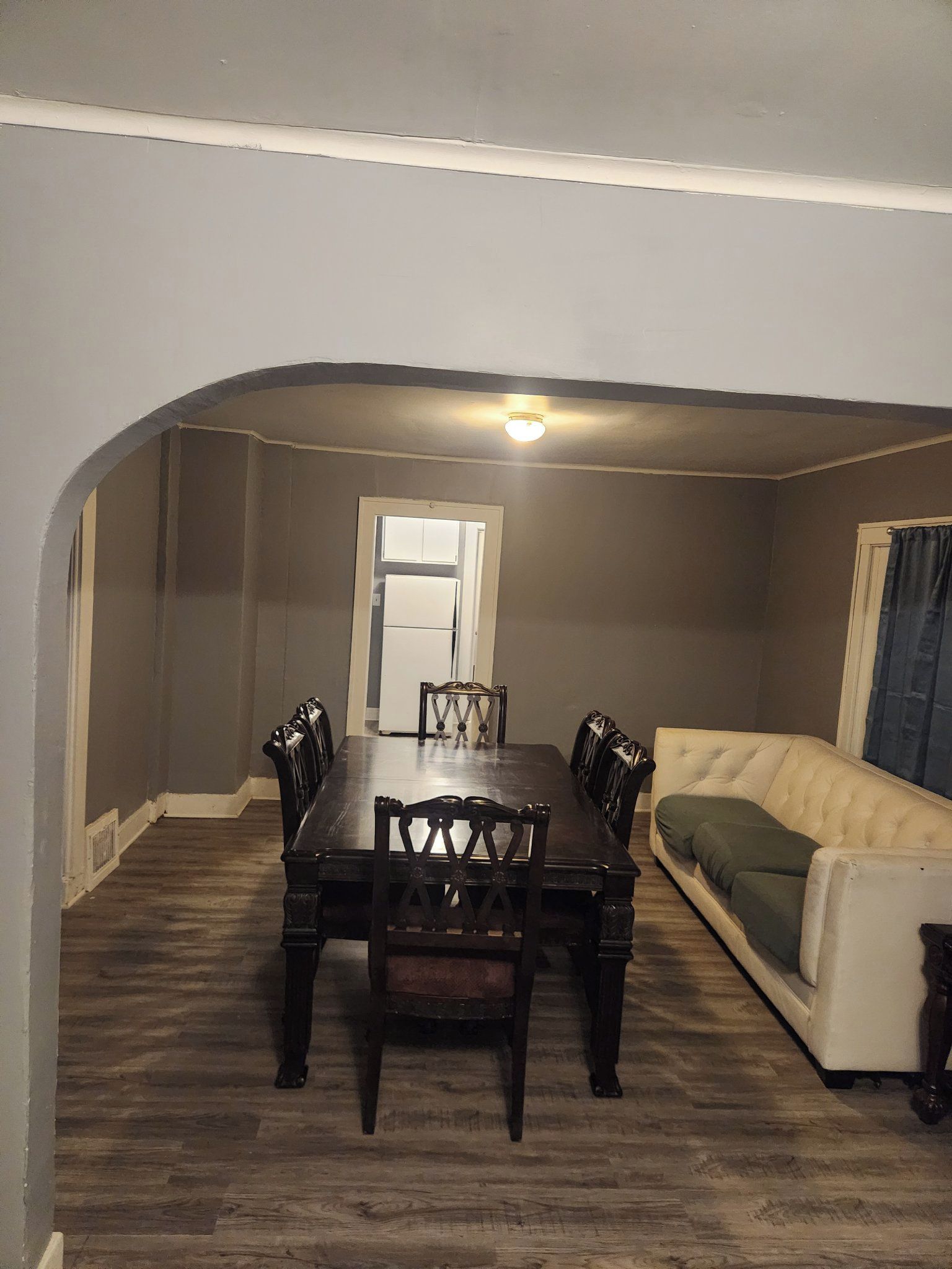 Un coin repas avec une table et des chaises en bois, un réfrigérateur blanc et un canapé beige.