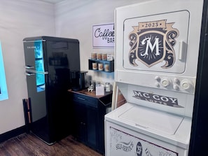 A self-service coffee machine with a 25 cent charge, a black refrigerator, and a coffee bar with various coffee products. - Suite Carolyn located in the historic Mc Coy Place Lofts. (Cave City)