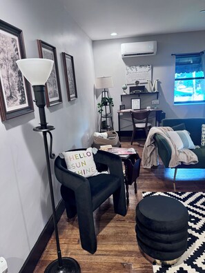 Un salon moderne avec un fauteuil noir, une lampe sur pied, un pouf noir et un tapis à motifs.