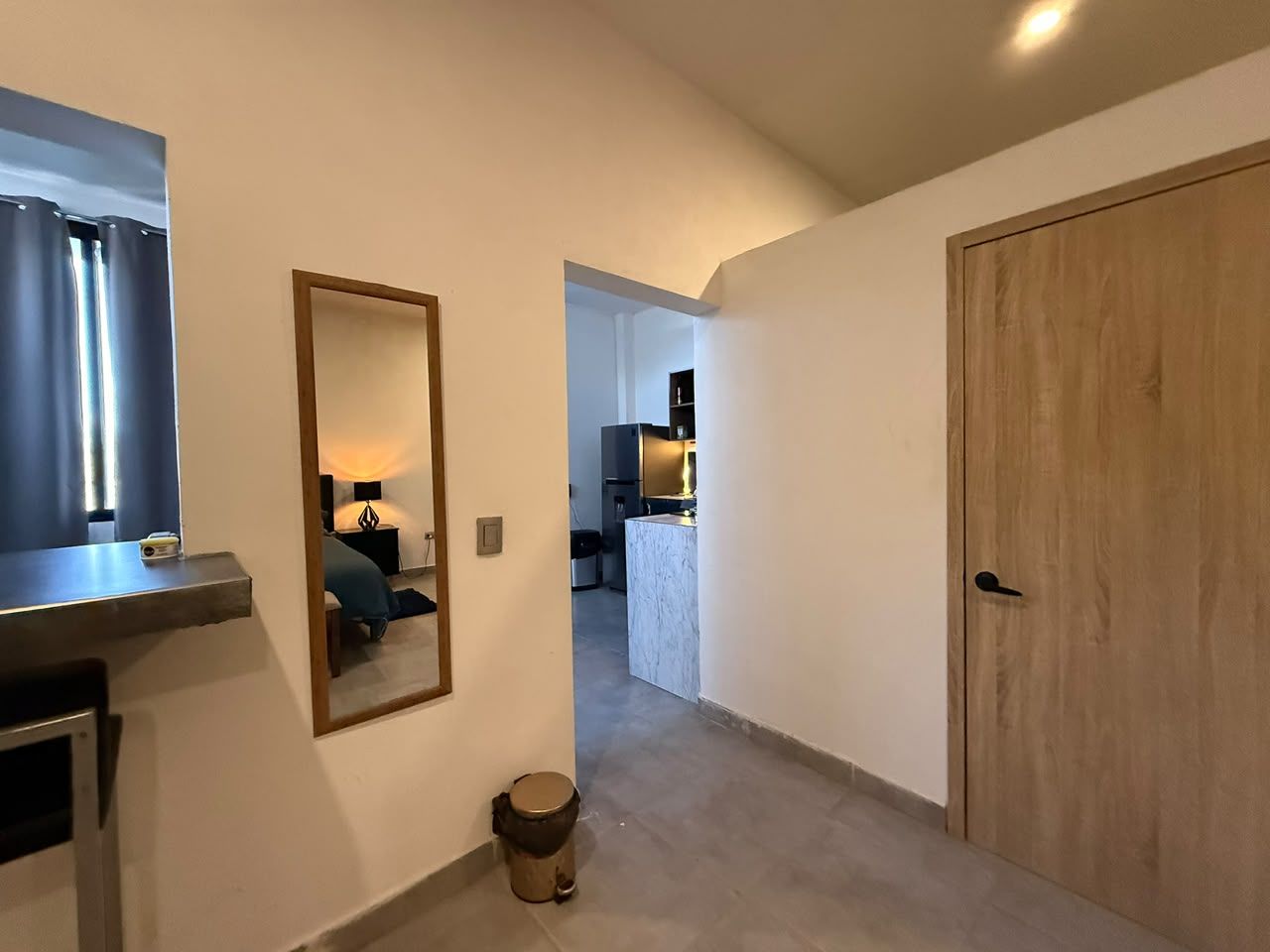 Corredor que dá para um quarto com cama, banheiro e espaço de cozinha.