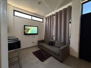 A living room with a flat-screen TV mounted on the wall, a sofa, a coffee table, and a small kitchen area with a microwave. - New Listing (El Centenario)