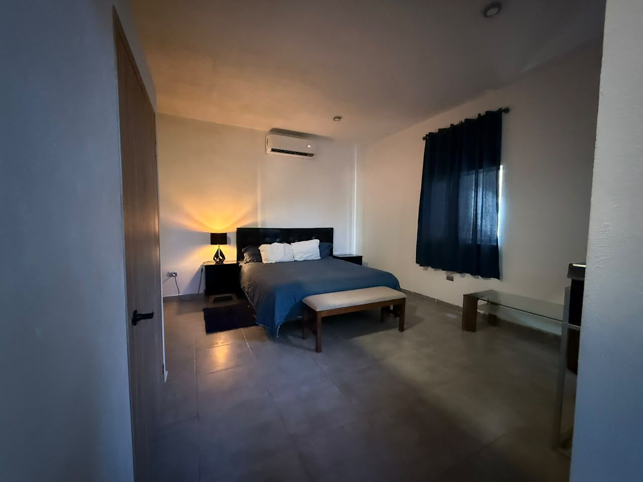 Une chambre à coucher avec un lit, une table de chevet, un banc et une fenêtre avec des rideaux.