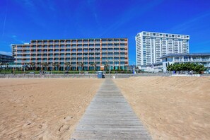 A beachside hotel with a long wooden boardwalk leading to the beach, a large building with multiple balconies, and a tall white building in the background. - Oceanfront Studio: Boardwalk, Beach, & Pool Views
WiFi & Free Parking Included (Virginia Beach)