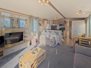 A modern living room with a flat-screen TV, a sofa, a coffee table, and a dining area with a table and chairs. - The Alderley - Ty Mawr, Towyn, Wales (Towyn)