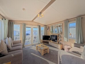 Un salon comprenant un ensemble de canapés, un téléviseur, une table basse et une vue sur l’extérieur.