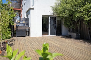 A modern outdoor patio with a barbecue grill, a sliding glass door, and a wooden deck. - School house by the bay, beach walks, large yard, happy paws (Rippleside)