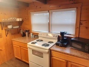 A kitchen with a white stove, a black microwave, and wooden cabinets.