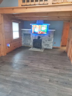 A room with a stone fireplace, a television mounted above it, and a wooden floor.