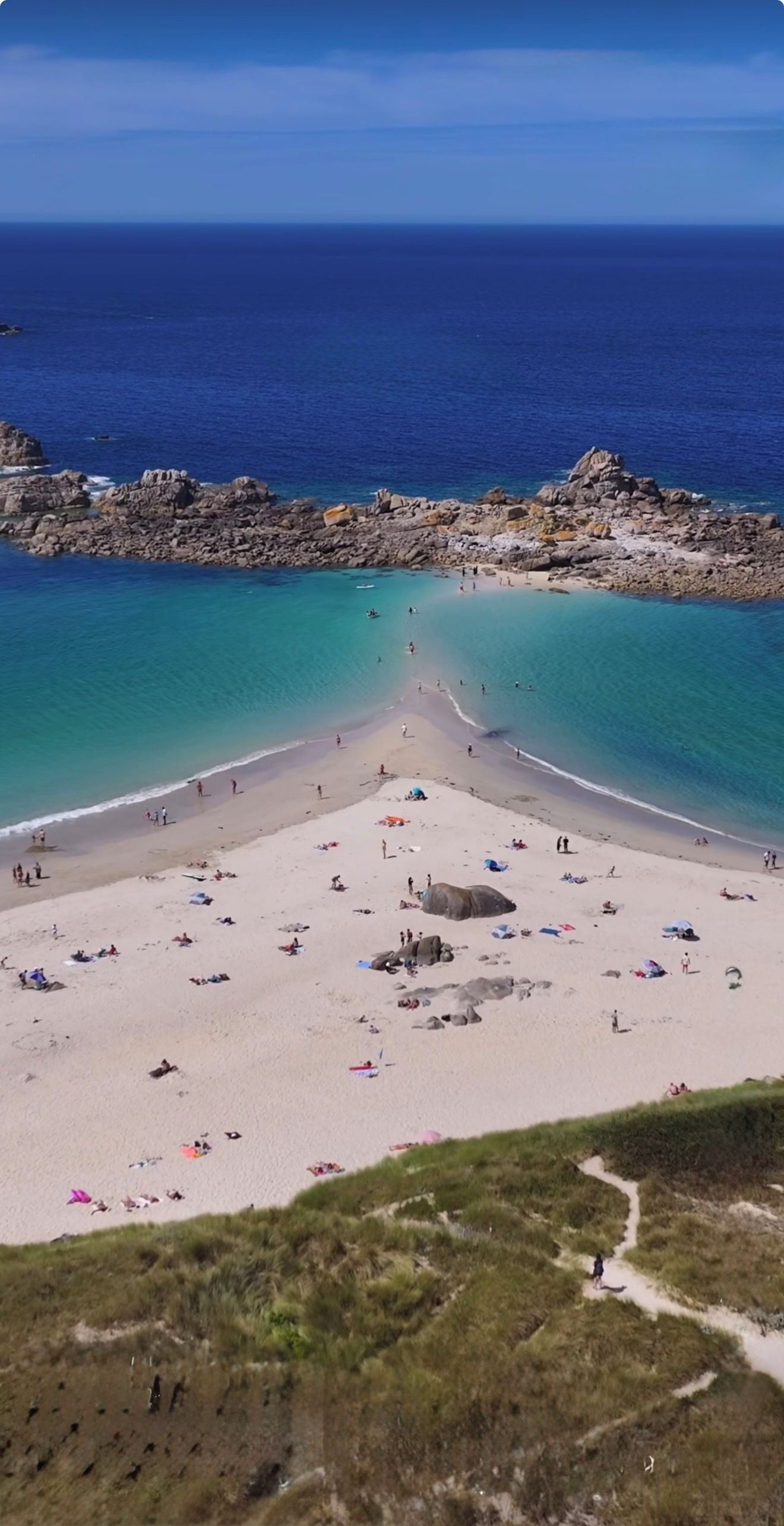 A beach with clear turquoise waters, rocky formations, and a sandy area with people and umbrellas.