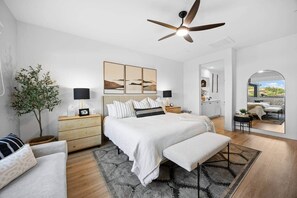 A modern bedroom with a large bed, bedside tables, a ceiling fan, and a view through a glass door to an outdoor area. - Terra Sol Coachella | Saltwater Pool, Spa & Firepit (Coachella)