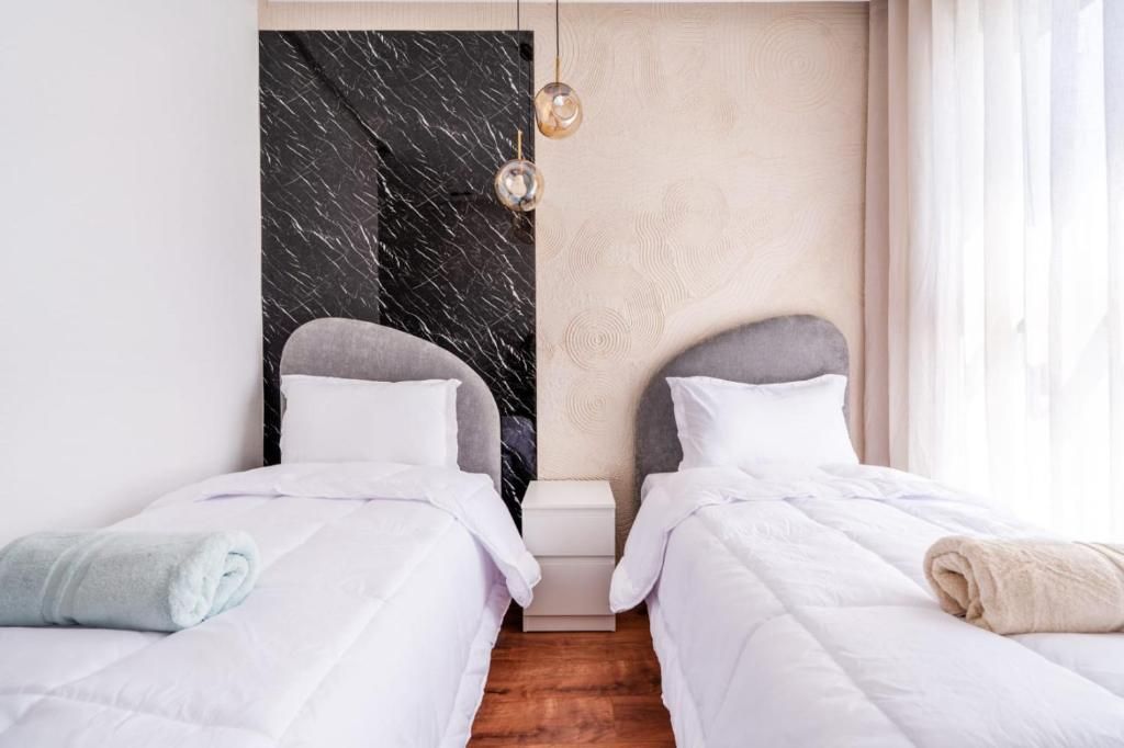 Habitación de hotel con dos camas, una pared decorada con mármol, una pared de paneles de madera y una lámpara colgante.