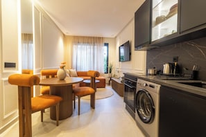 Eine moderne Küche mit eingebautem Backofen und Mikrowelle, ein Essbereich mit rundem Tisch und orangenen Stühlen sowie eine Wohnbereich mit Sofa und Couchtisch.