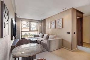 Ein modernes Wohnzimmer mit einer Eckcouch, einem runden Glastisch und einem an der Wand befestigten Fernseher.