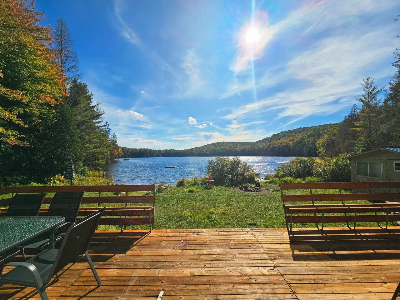 Een houten terras met een tafel en stoelen, met uitzicht op een meer met een boot in de verte.