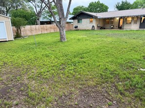 Ein Garten mit Rasen, einem Baum und einem Haus mit Garage und Gartenhaus.