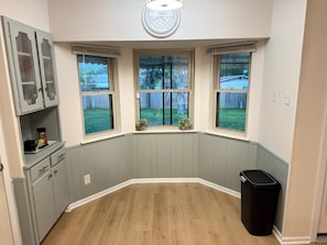 Ein Eckzimmer mit Erkerfenster, einem Mülleimer und einer kleinen Küchenzeile.