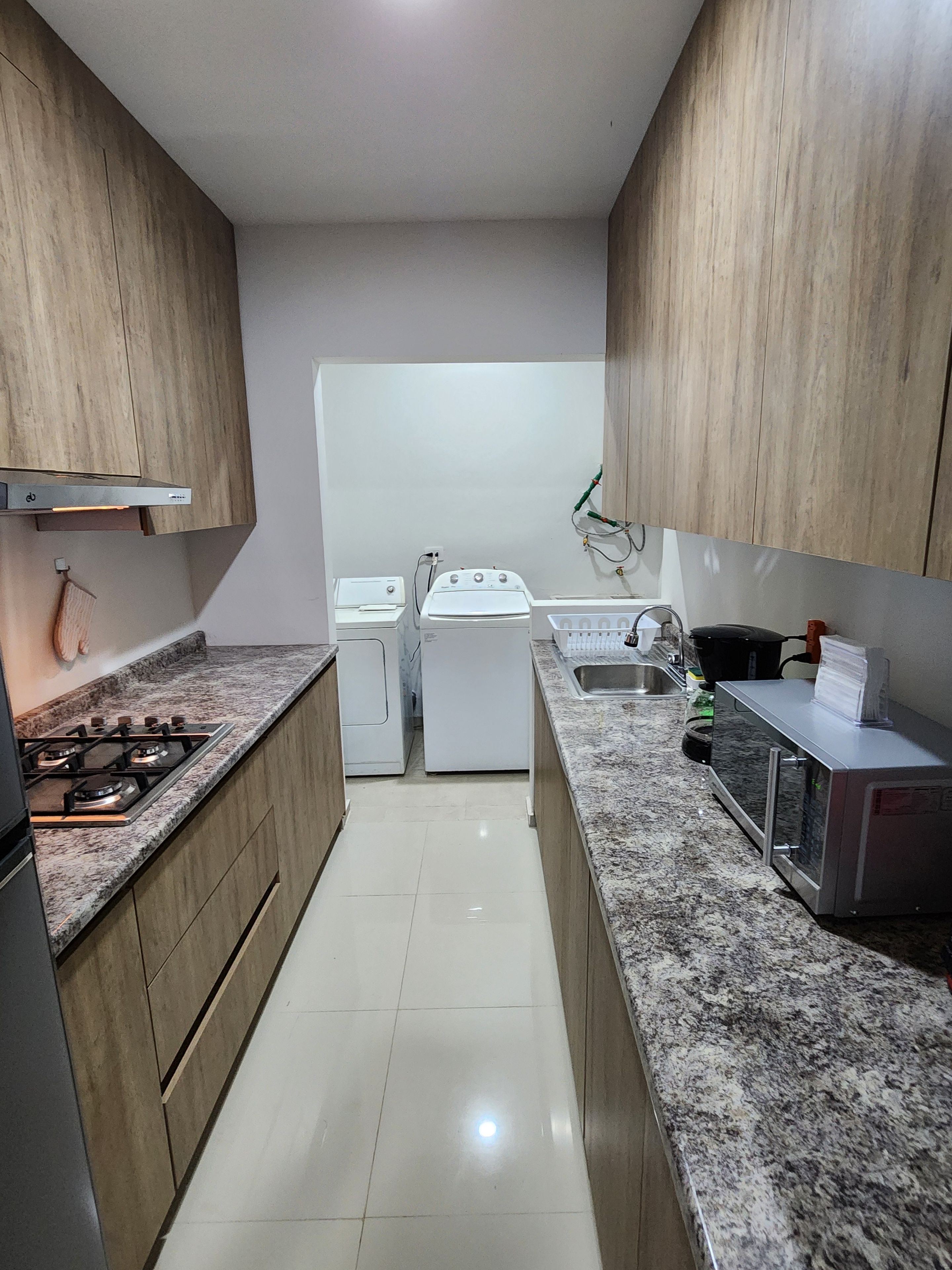 Una cocina con armarios de madera, una estufa a gas, un microondas y un lavamanos.