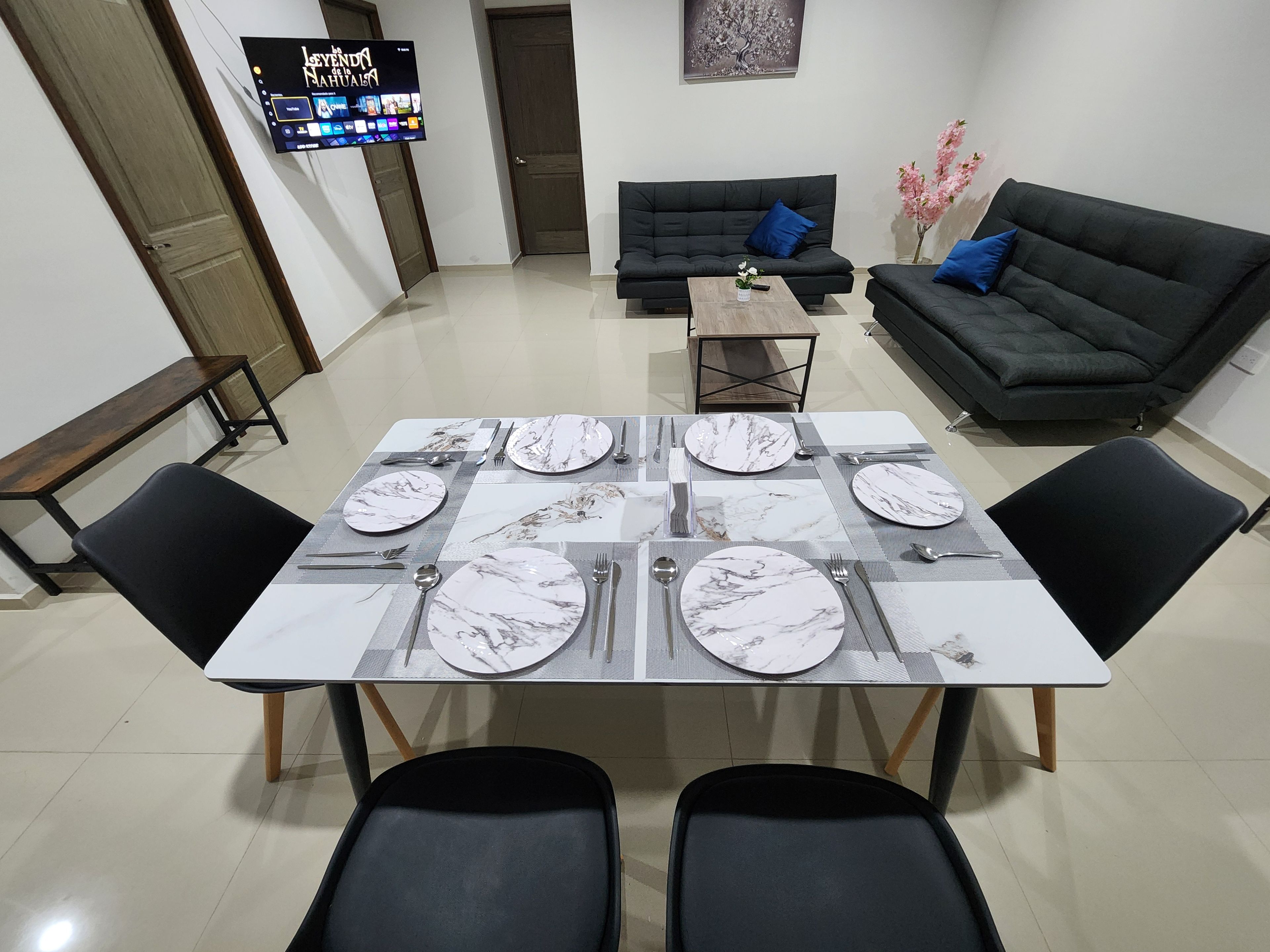 Un coin repas avec une table dressée pour quatre personnes, un canapé et un téléviseur fixé au mur.