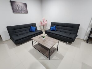 Une pièce avec deux canapés noirs, une table basse en bois et un vase rempli de fleurs.