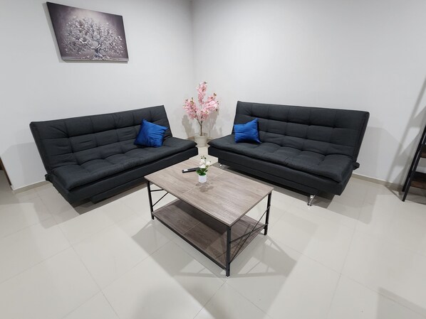 Una habitación con dos sofás negros, una mesa de centro de madera y un jarrón con flores.