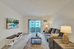 A modern living room with a pool view, a sofa, a coffee table, and a TV mounted on the wall. - One block from the beach - Newly furnished 1 bedroom condo (Fort Lauderdale)