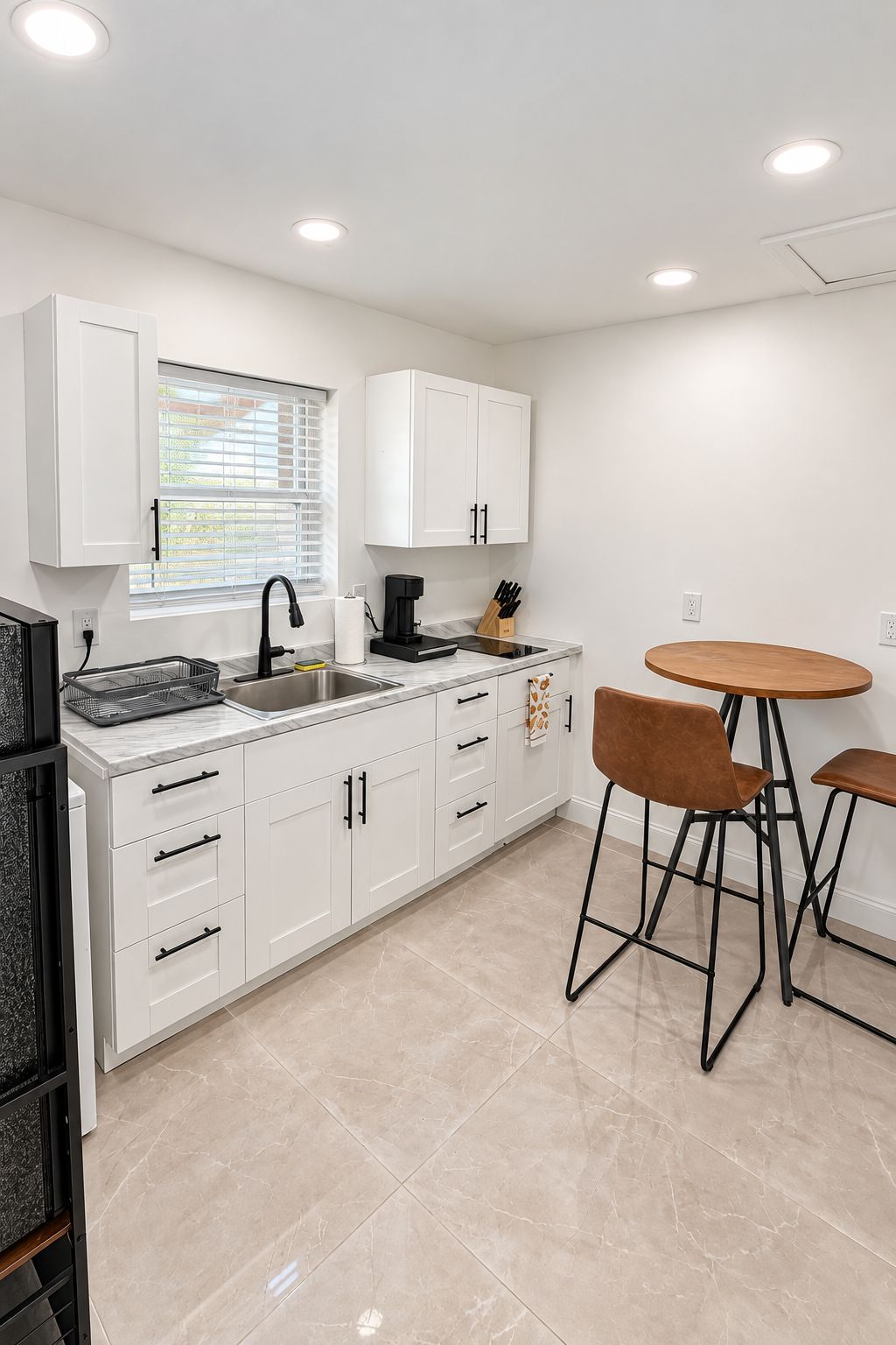 A modern kitchen with white cabinets, a marble countertop, a coffee maker, and a round wooden table with two chairs.